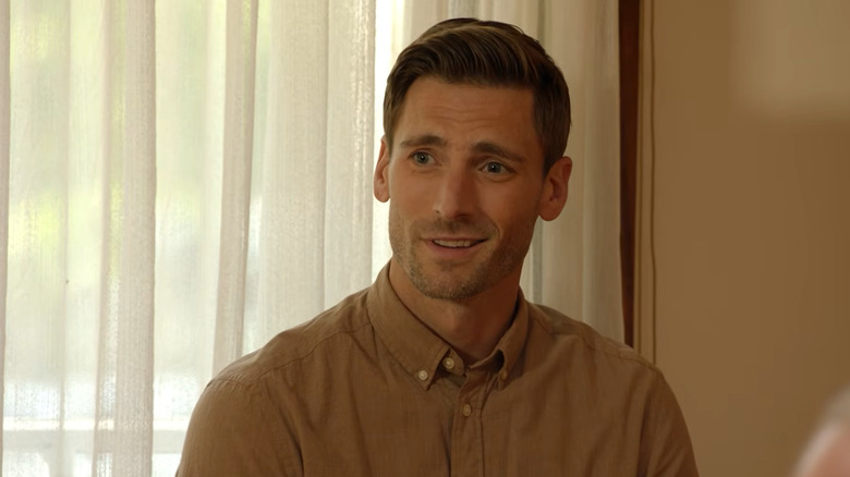 Screenshot of Hallmark movie "Sweet Autumn" starring Andrew W. Walker. Walker is smiling at another character off-screen and wearing a tan/light-brown buttoned-up shirt.