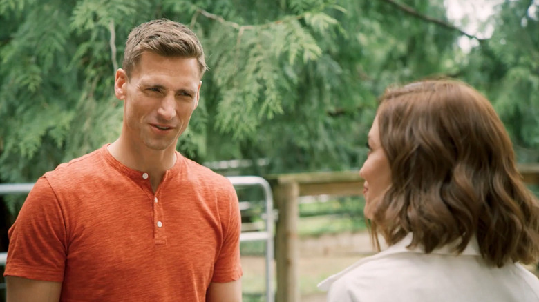 Screenshot of Hallmark movie "The 27-Hour Day" starring Andrew W. Walker and Autumn Reeser. The two co-stars are talking next to a pig pen with visible fences and gates.