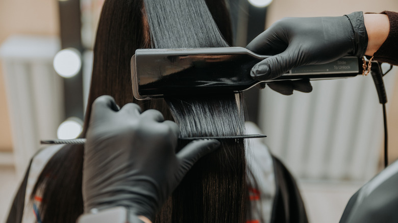 Dark hair being flatironed by someone wearing gloves