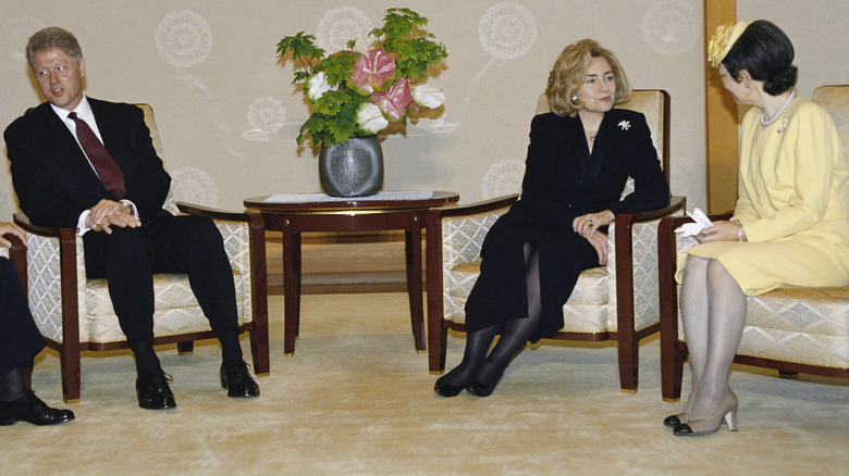 Hillary Clinton seated in all black next to a woman wearing yellow