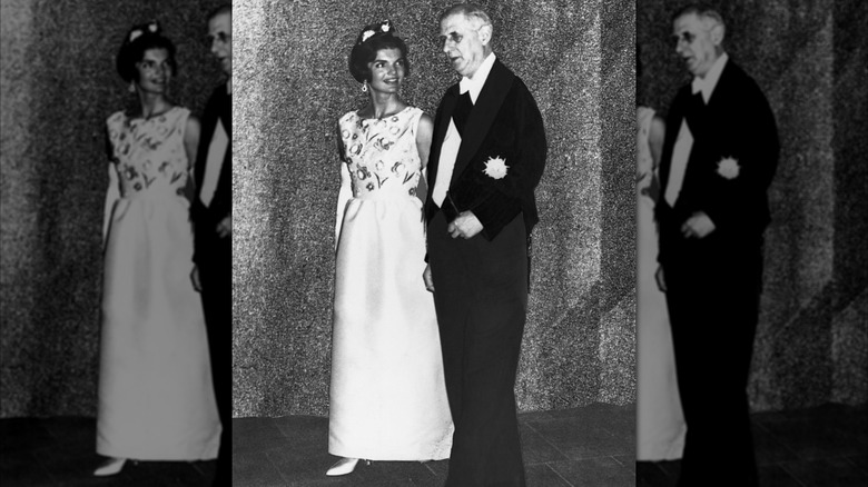 Jacqueline Kennedy wearing a white gown while walking with a French diplomat