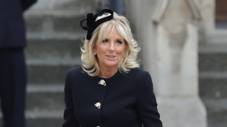 Jill Biden gazing into the distance while wearing a black jacket and a swirly fascinator
