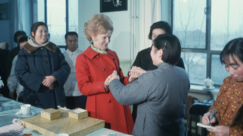 Pat Nixon holding the hands of a woman while visiting China in her red peacoat