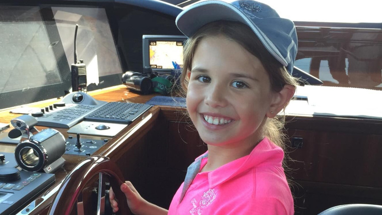 image of a young Kai Trump smiling as she holds the wheel of a boat