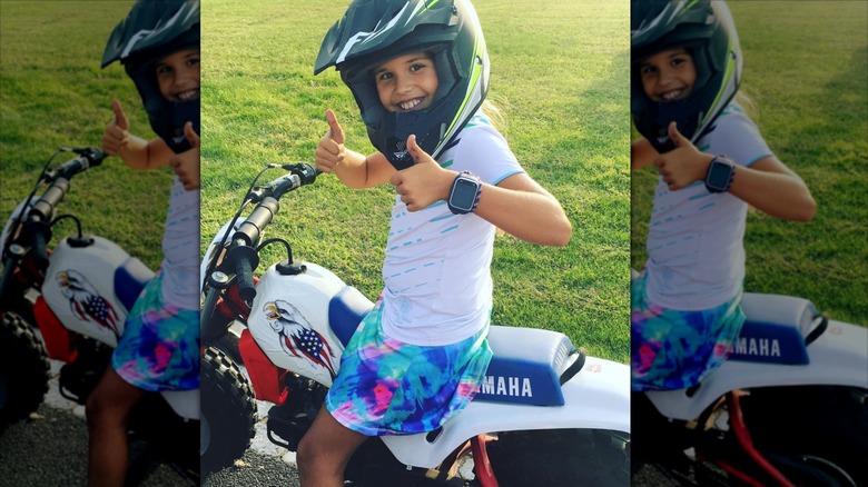 image of a young Kai Trump with her thumbs up and smiling with a helmet while sitting on top of a mini-motorbike