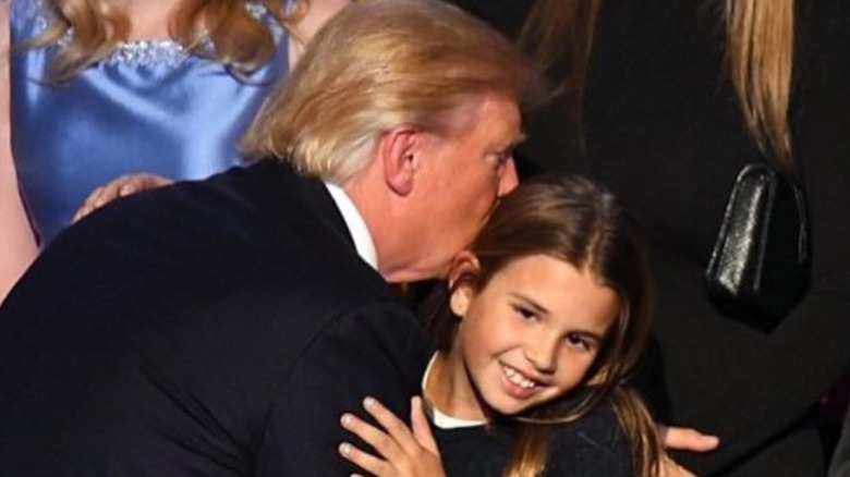 image of a young Kai Trump receiving an awkward kiss from Donald Trump