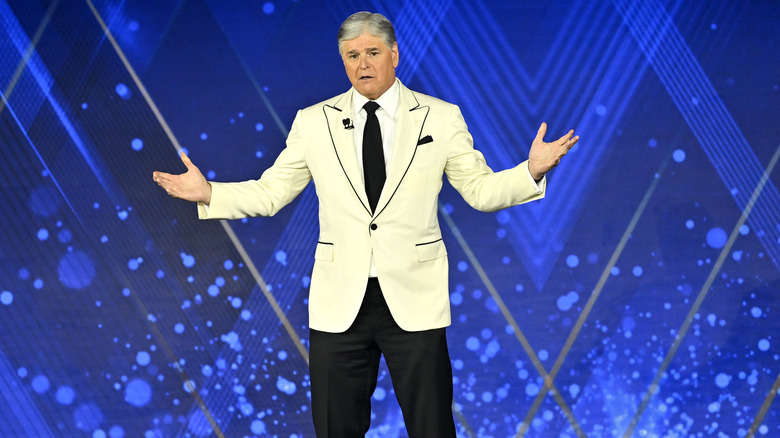 Sean Hannity wearing a white blazer and standing with his arms outstretched