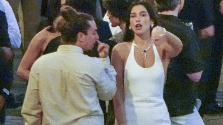 Dua Lipa in a white dress speaking to a friend at her pre-wedding party.