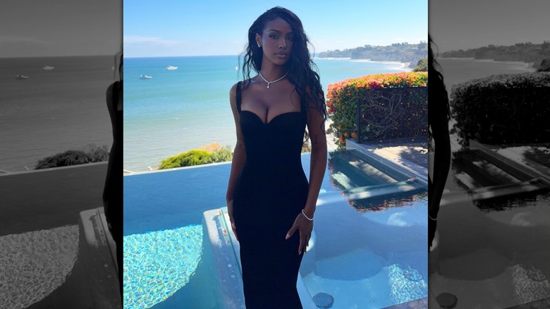 Justine Skye in a figure-hugging black dress, standing next to a pool.