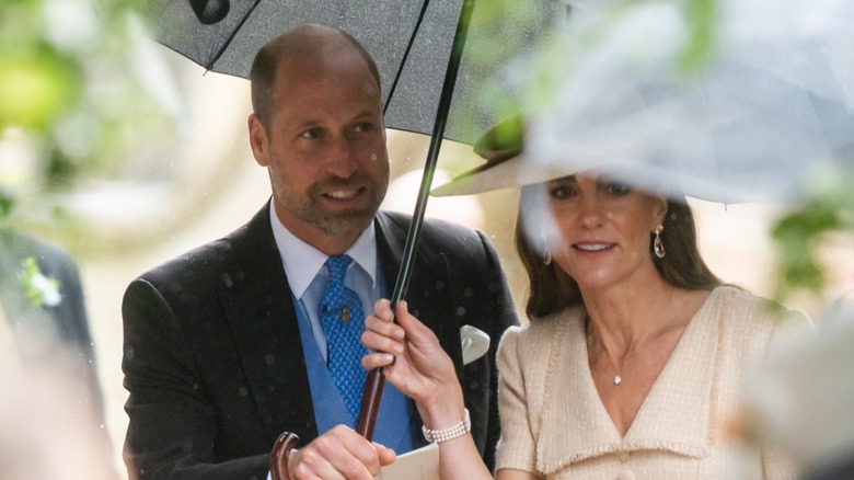 Prince William, in a blue waistcoat and tie, sheltering under an umbrella with Kate Middleton.