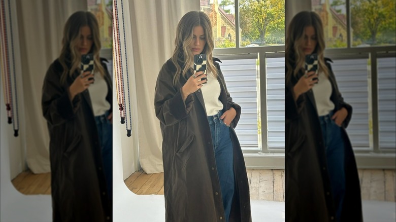 Emily Michelle in a brown trench coat and jeans taking a selfie