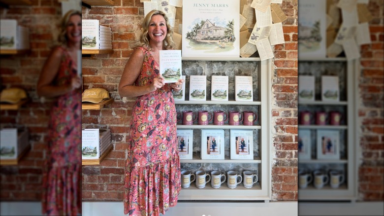 Jenny Marrs in a pink dress holding her book in front of a brick wall