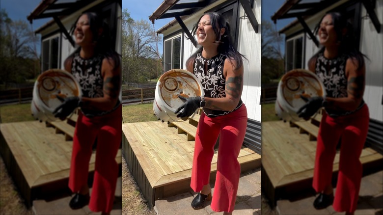 Margo Fairchild in red pants and a black and white top shaking a large can of paint