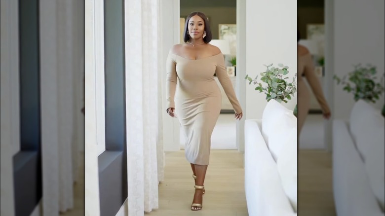 Noel Collier in a nude dress walking down a hallway