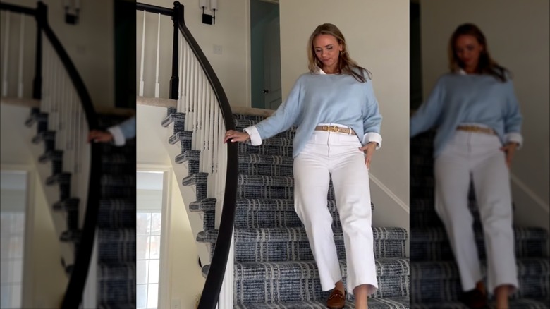 Tamara Day walking down the stairs in a blue sweater and white pants