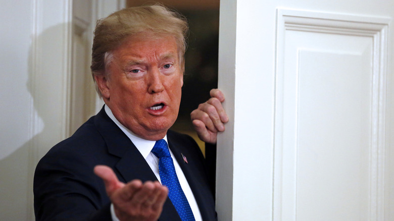 Donald Trump gestures to the press from the doorway of the Oval Office