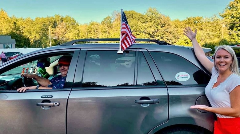 Karoline Leavitt posing next to a car with an American flag on it