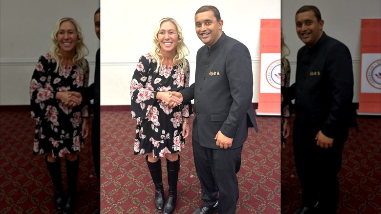 Marjorie Taylor Greene smiles while shaking hands with a man in a gray suit