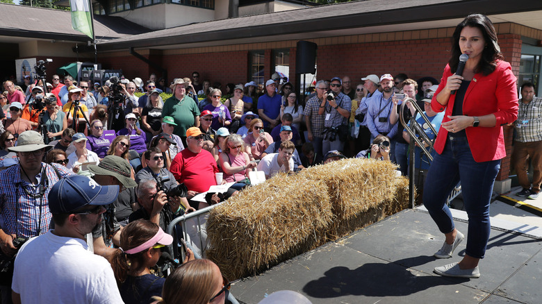 Tulsi Gabbar speaks onstage in a red blazer