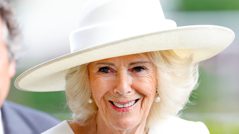Close-up of Queen Camilla smiling in white, wide-brimmed hat