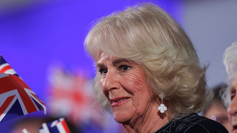 Queen Camilla smiling in audience surrounded by U.K. flags