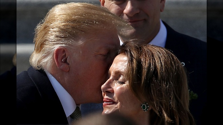 Nancy Pelosi closing her eyes and smiling outdoors as Donald Trump kisses her on the cheek in March 2019.