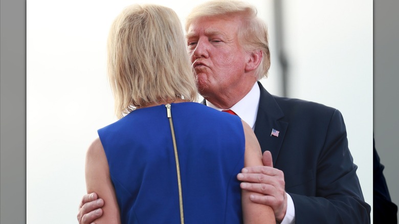 Donald Trump squinting and puckering his lips while grabbing the arms of Mary Miller, who has her back to the camera, at a 2022 rally