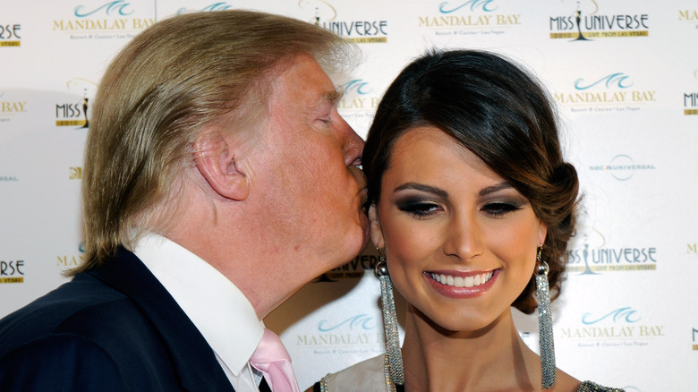 Donald Trump kissing Miss Universe 2009 Stefania Fernandez above the ear as she looks down and smiles awkwardly.