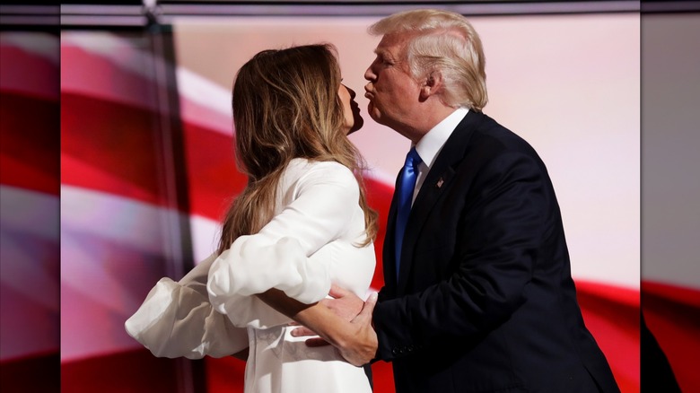Donald Trump grabbing Melania Trump's waist and leaning forward to kiss her while she grabs his wrists at the 2016 RNC.