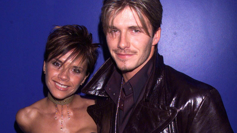 Victoria and David Beckham smile at the camera against a blue background