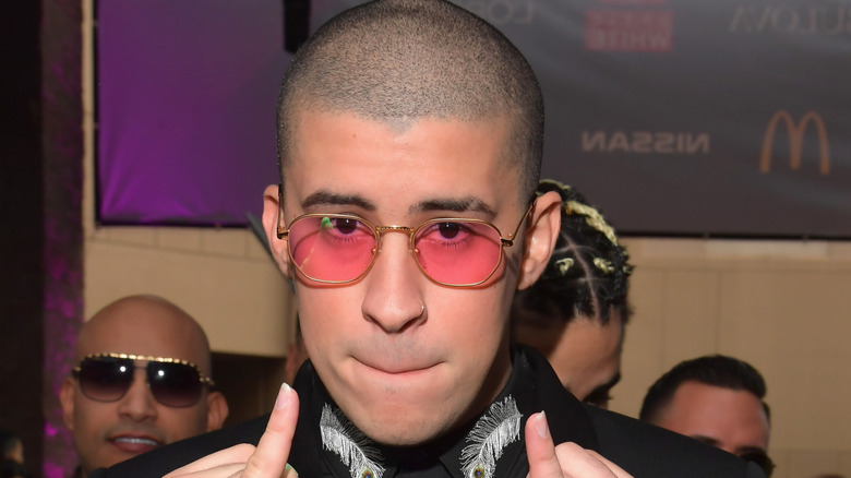 Bad Bunny, in rose-colored glasses, purses his lips and holds up his pinkies.