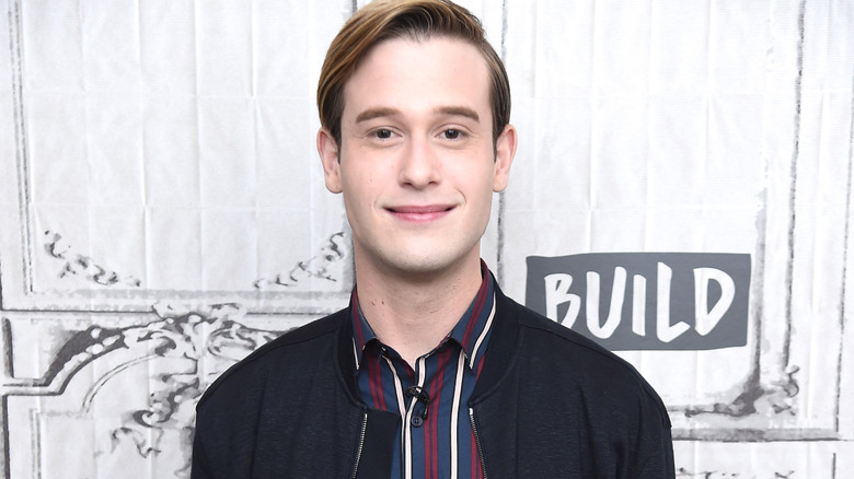 Hollywood medium Tyler Henry smiles closed lip on the red carpet in a blue striped button down