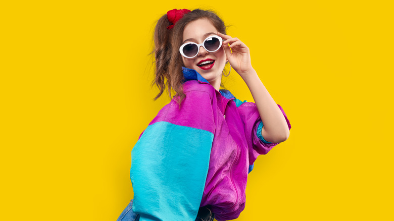 Woman posing, wearing multi-color track jacket and white sunglasses