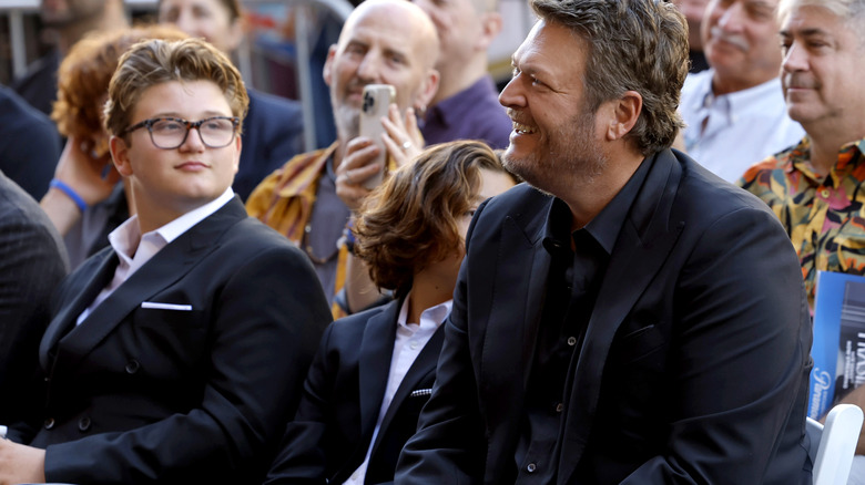 Zuma Rossdale and Blake Shelton sitting next to each other wearing suits