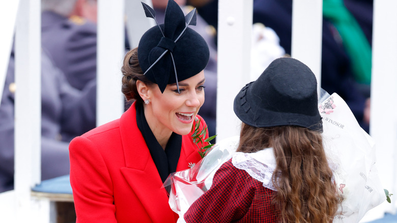 Kate Middleton in a black fascinator receiving flowers from child
