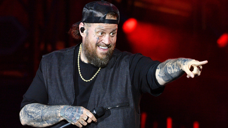 Jelly Roll with a mic in his hand pointing at an audience member in an all-black outfit