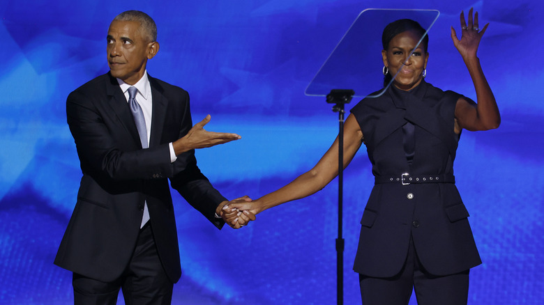 Barack Obama pointing at Michelle Obama as she waves to the crowd