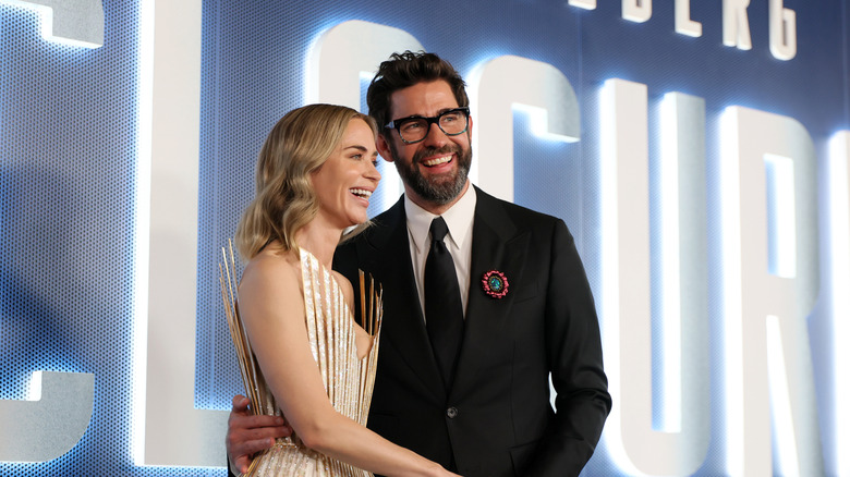 Emily Blunt and John Krasinski in front of a blue and white background
