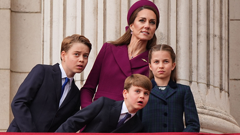 Princess Charlotte standing up straight and looking serious as her mother and brothers look on curiously at a display