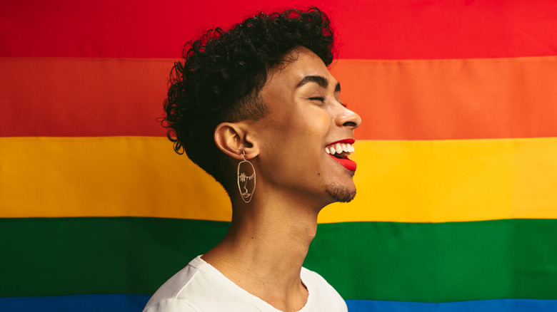 Person standing in front of a Pride flag in makeup