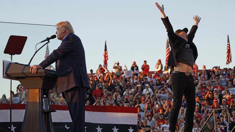 Elon Musk jumping while Donald Trump gives a speech