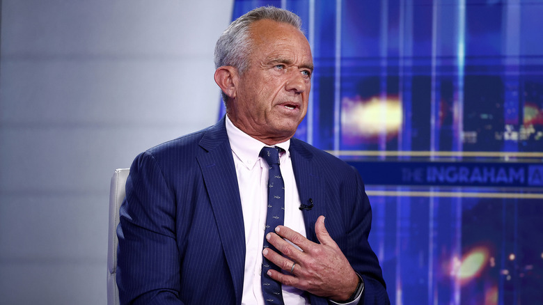RFK Jr. talking in a suit while raising his hand