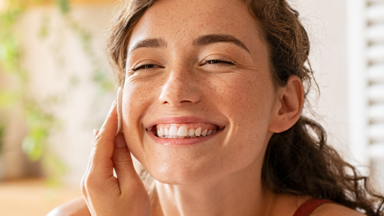 Woman with curly hair smiling while washing her face