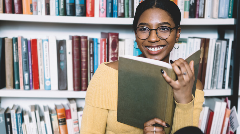 Woman sitting in front of library shelves, smiling with open book