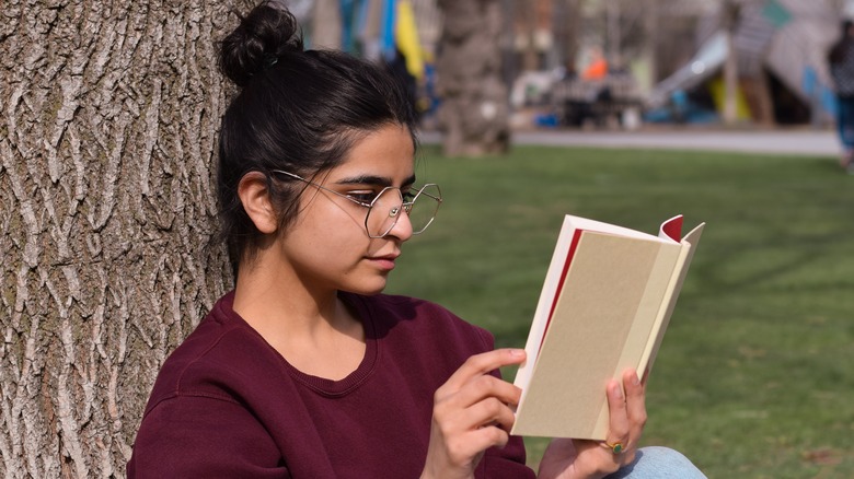 Young woman reading a book against a tree