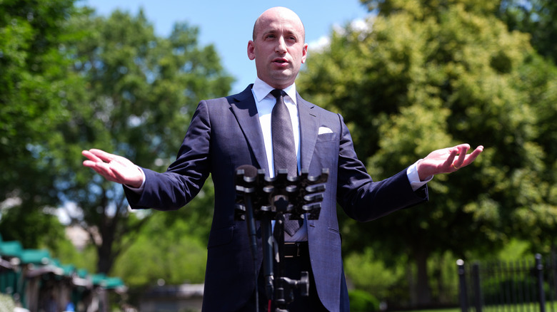 Stephen Miller opening his arms as he addresses a crowd in a navy blue suit