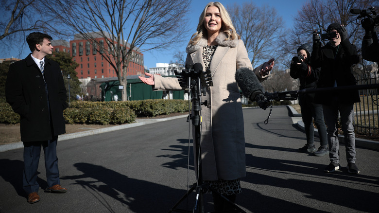 Karoline Leavitt talking to reporters outside of the white house in a long tan trench coat.