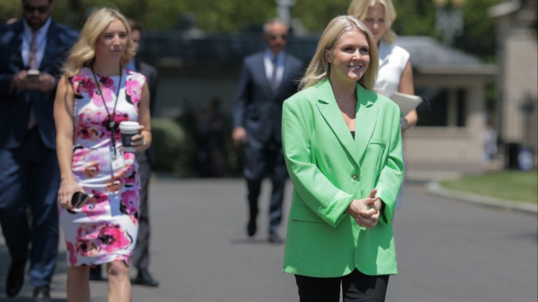 Karoline Leavitt smiling while wearing a large green blazer and black pants.
