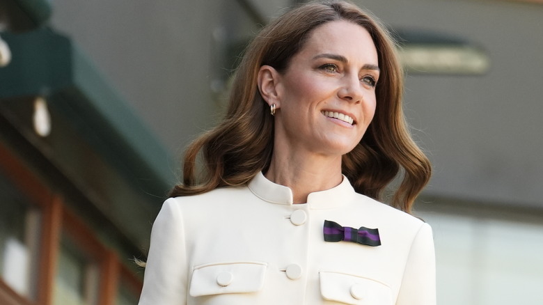 Princess Catherine smiling in a white outfit with a purple bow