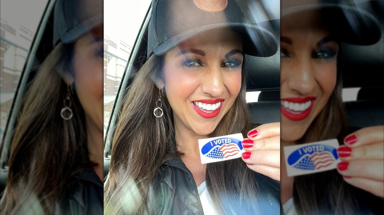 Lauren Boebert smiling without glasses while holding an 'I Voted' sticker.